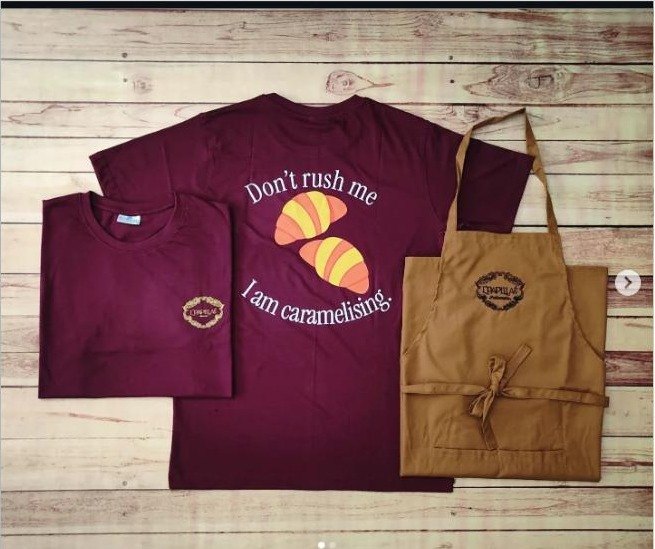 Bakery uniforms, maroon t-shirts printed 'Don't rush me, I am caramelising' with brown canvas aprons and embroidered crest