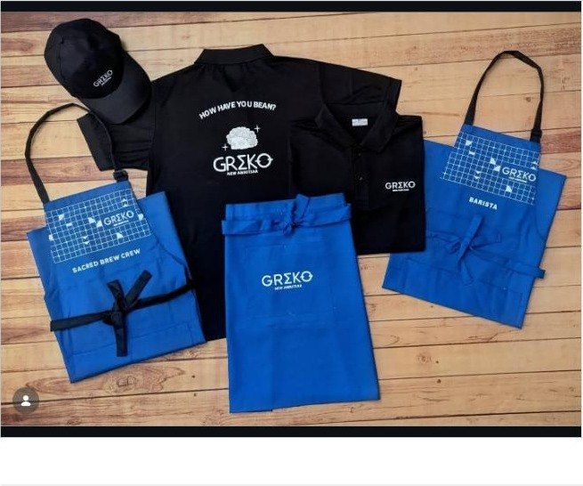 Custom coffee shop uniforms for Greko Espresso Bar, Amritsar, black polos and caps with electric blue canvas aprons embroidered 'Sacred Brew Crew'