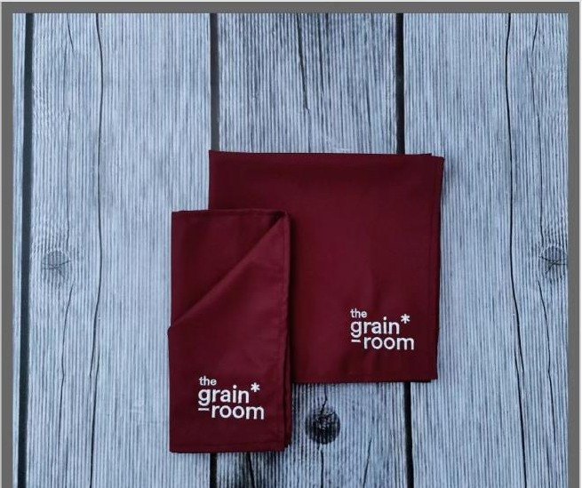 Deep maroon custom table napkins printed with The Grain Room logo, folded and stacked